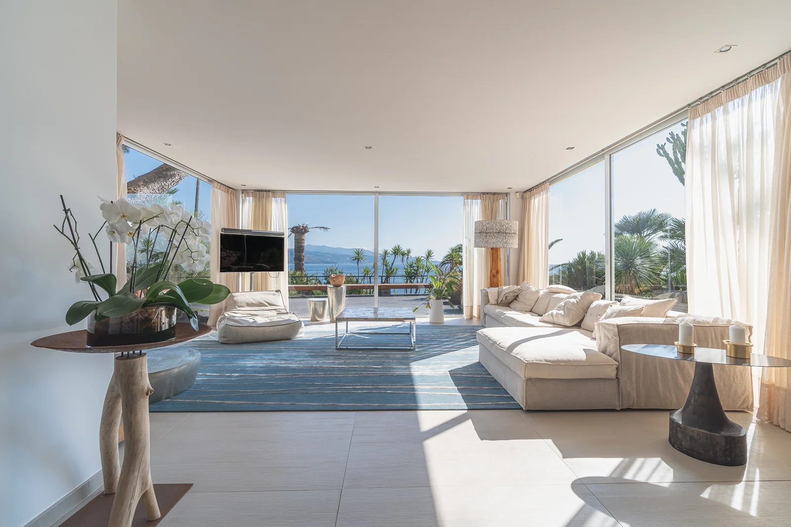 Salon d'une belle villa, lumineux, clair et épuré, dans des tons blanc, beige et doré avec vue sur la mer dans un contexte de photos et vidéos immobilières.