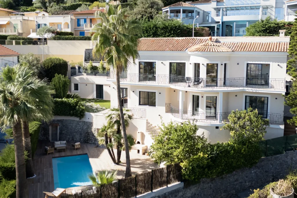 Vue par drone d'une grande et belle villa à Roquebrune, avec plusieurs étages, palmier et verdure tout autour, et une piscine entourée d'un parquet en bois, dans le cadre d'un shooting de vidéos immobilières